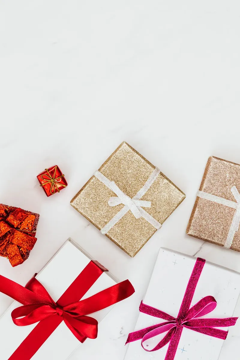 Gold glitter gift boxes with white ribbons beside red and white gift packaging